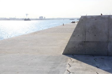 Sakin mavi suyun yanında uzanan güneşli beton iskele.