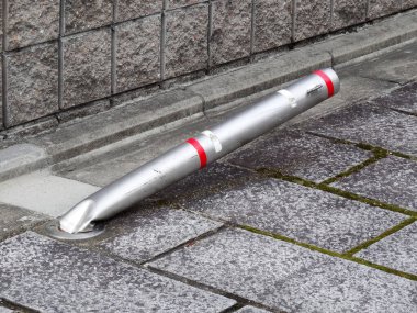 Gri taş kaldırımda uzanan eğri metal bir direk.