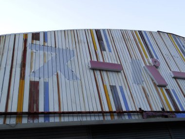 Eski bükülmüş metal bina cephesini kaplayan soluk renkli çizgiler