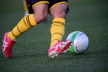 Bir futbolcu sahada futbol topunu tekmeliyor.