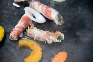 Grilling bacon wrapped vegetables beside sliced onion and pumpkin