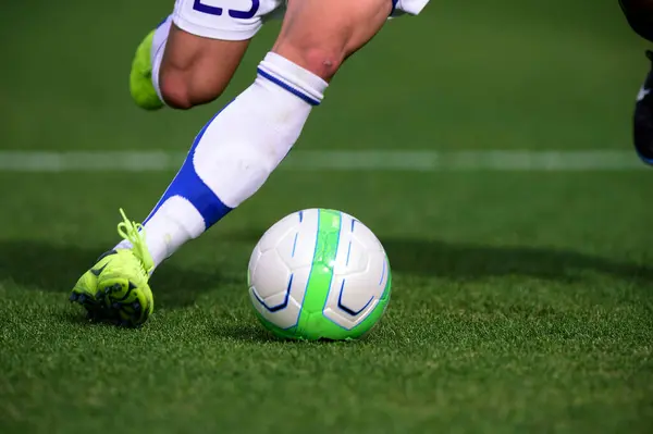 Bir futbolcu sahada futbol topunu tekmeliyor.