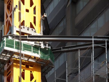 Sarı inşaat vinci modern binanın yakınındaki iskeleyi destekliyor.