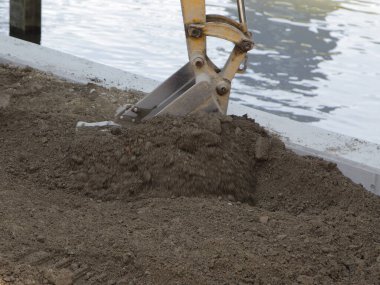Kazıcı sakin su kenarında kahverengi toprak kazıyor