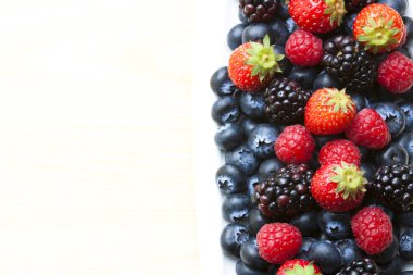 Çeşitli taze meyveler. Beyaz arka planda yaban mersini, ahududu ve böğürtlen