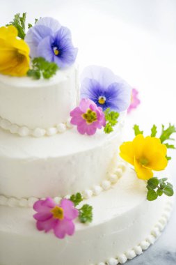 Krema ve taze çiçeklerle süslenmiş beyaz düğün pastası..              