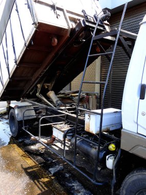 Endüstriyel çöp kamyonu, dış bina yakınlarında malzeme boşaltıyor.