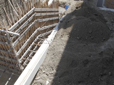 Büyük toprak yığınının yanında beton temeli destekleyen ahşap iskeleler.