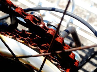 Kapalı çekimde paslı bisiklet zinciri ve metal parmaklıklar görünüyor.