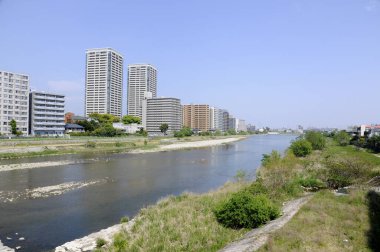 Açık mavi gökyüzünün altında nehir boyunca uzanan uzun modern binalar.