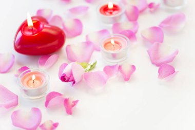 Beyaz arka planda pembe çiçek yapraklarıyla yanan güzel mumlar.        