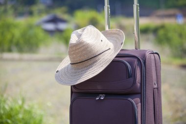 Açık havada duran hasır şapkalı bavul, seyahat kavramı.