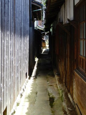 Güneş ışığı parlayan ahşap binalar arasında dar bir sokak.