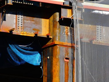 Mavi kumaş ve ağlarla kaplı paslı metal kirişler.