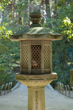 Yeşillik ormanda eğimli patikanın yanında duran taş fener.