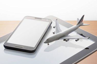 Dijital tablet bilgisayarda uçak modeli ve ahşap masada akıllı telefon 