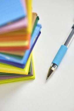 Üst üste dizilmiş renkli not kağıtları ve beyaz arkaplandaki kalemlerin yakın plan görünümü 