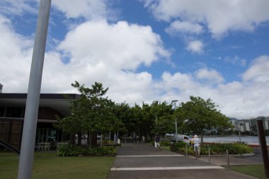 Ağaçlar ve binalarla dolu bir rıhtımda yürüyen insanlar