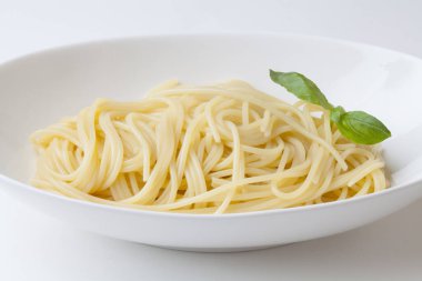 Beyaz tabakta fesleğenli makarna.