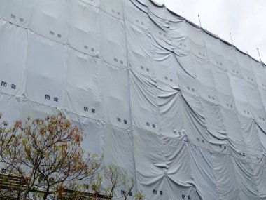 Açık havada beyaz koruyucu inşaat brandalarıyla kaplı büyük bir bina.