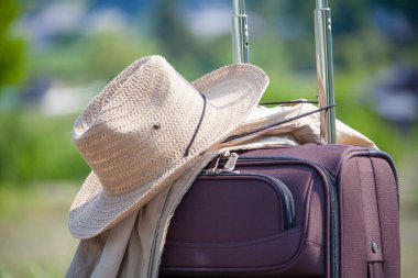 Açık havada duran hasır şapkalı ve ceketli bavul, seyahat konsepti.