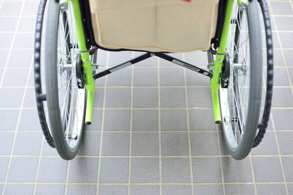 Closeup showing wheelchair wheels resting on tiled floor indoors