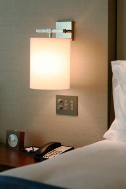 Modern duvar lambası telefon ve saatle komodinimi aydınlatıyor.