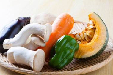 Tahta masadaki hasır sepetteki farklı sebzeler, yakın plan.