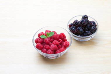 Tahta masada taze ahududu ve böğürtlen kaseleri.         