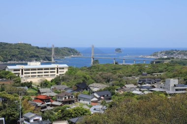 Sahil kasaba binaları, mavi denize bakan yemyeşil ağaçlarla çevrili.
