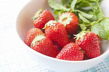 Taze olgun çilekler ve beyaz bir masada nane yaprakları.