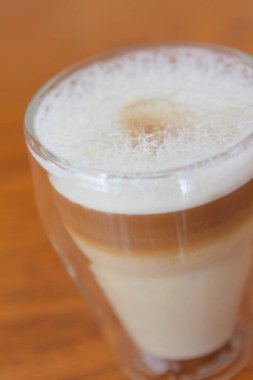 Ahşap masanın üzerindeki cam latte bardağının yakın görüntüsü.     