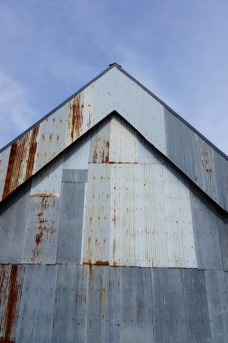 Yıpranmış metal bina kaplaması mavi gökyüzüne karşı pas gösteriyor.