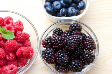 Çeşitli taze meyveler. Yaban mersini, ahududu ve böğürtlen kaselerinde