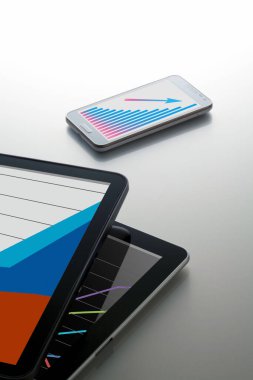 Gri arkaplan üzerinde iş grafikleri olan modern Dijital Tabletlerin ve telefonun yakın plan görüntüsü       