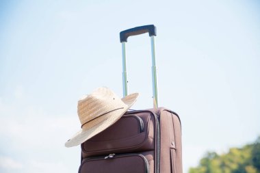 Mavi gökyüzüne karşı hasır şapkalı bavul, seyahat ve tatil konsepti.