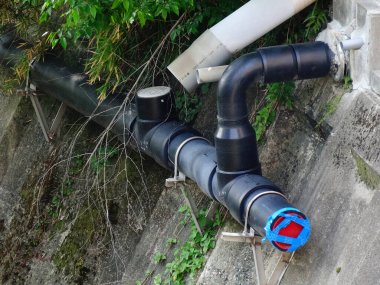 Beton duvar boyunca uzanan büyük siyah drenaj borusu.