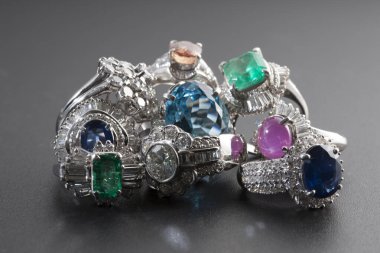 Zümrüt, safir, yakut ve akuamarinler gibi renkli değerli taşları olan yüzükler koyu bir yüzeyde zarifçe sergilenmektedir..