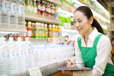 Yeşil önlüklü neşeli Japon kadın. Markette panosu olan gülümseyen bir işçi.