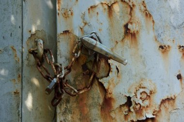Paslı metal zincir yıpranmış kapıyı sıkıca kilitliyor.