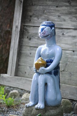 Seramik kappa heykeli dışarıda ahşap çitlerin yanında diz çöküyor.