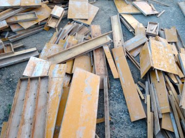 Dağılmış sarı ahşap kalaslar engebeli çakıl zeminde yatıyor.