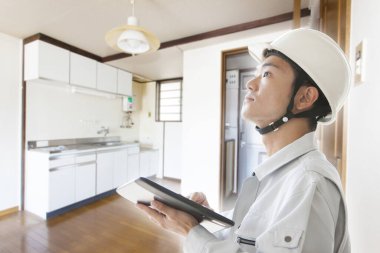 Genç Asyalı mühendis kasklı ve tabletli odada duruyor.  