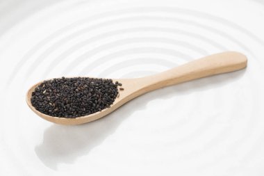 Beyaz arka planda kaşık içinde siyah fesleğen tohumları. 