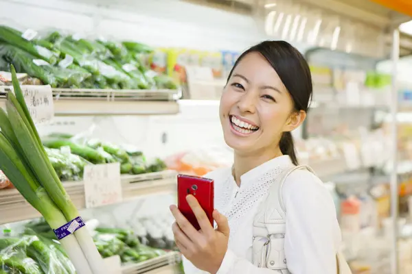 Uśmiechnięta Japonka Smartfonem Zakupy Sklepie Spożywczym Sprawdzanie Listy Zakupów Telefonie — Zdjęcie stockowe