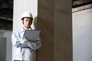 Üniformalı yakışıklı Japon inşaatçının portresi. İnşaat alanını pano ile inceliyor.