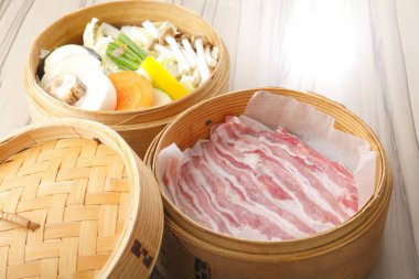 Domuz pastırması dilimleri ve çiğ sebzelerin masalardaki bambu kutularda çekilmiş bir mutfak fotoğrafı. 