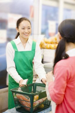 Yeşil önlüklü kadın işçi ve süpermarketteki müşteri.