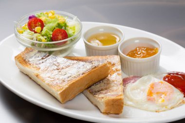 Yumurta, tost, salata ve sosla nefis bir kahvaltı. Sıcak bir yemek ortamında beyaz bir tabakta servis ediliyor.