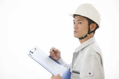 Üniformalı yakışıklı Japon inşaatçının portresi. İnşaat alanını pano ile inceliyor.